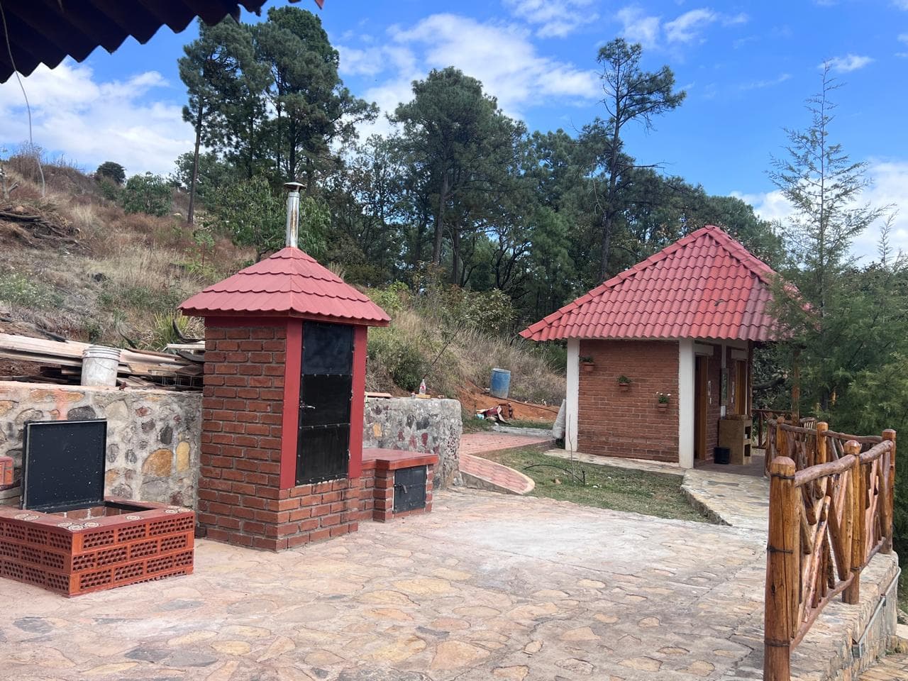 Vista general de un área exterior con horno de leña, construcciones de ladrillo, cubiertas rojas y acabados rústicos.